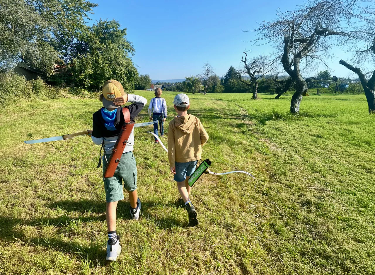 Kinder auf einer Wiese unterwegs zum Bogenschießen Kinder auf einer Wiese unterwegs zum Bogenschießen