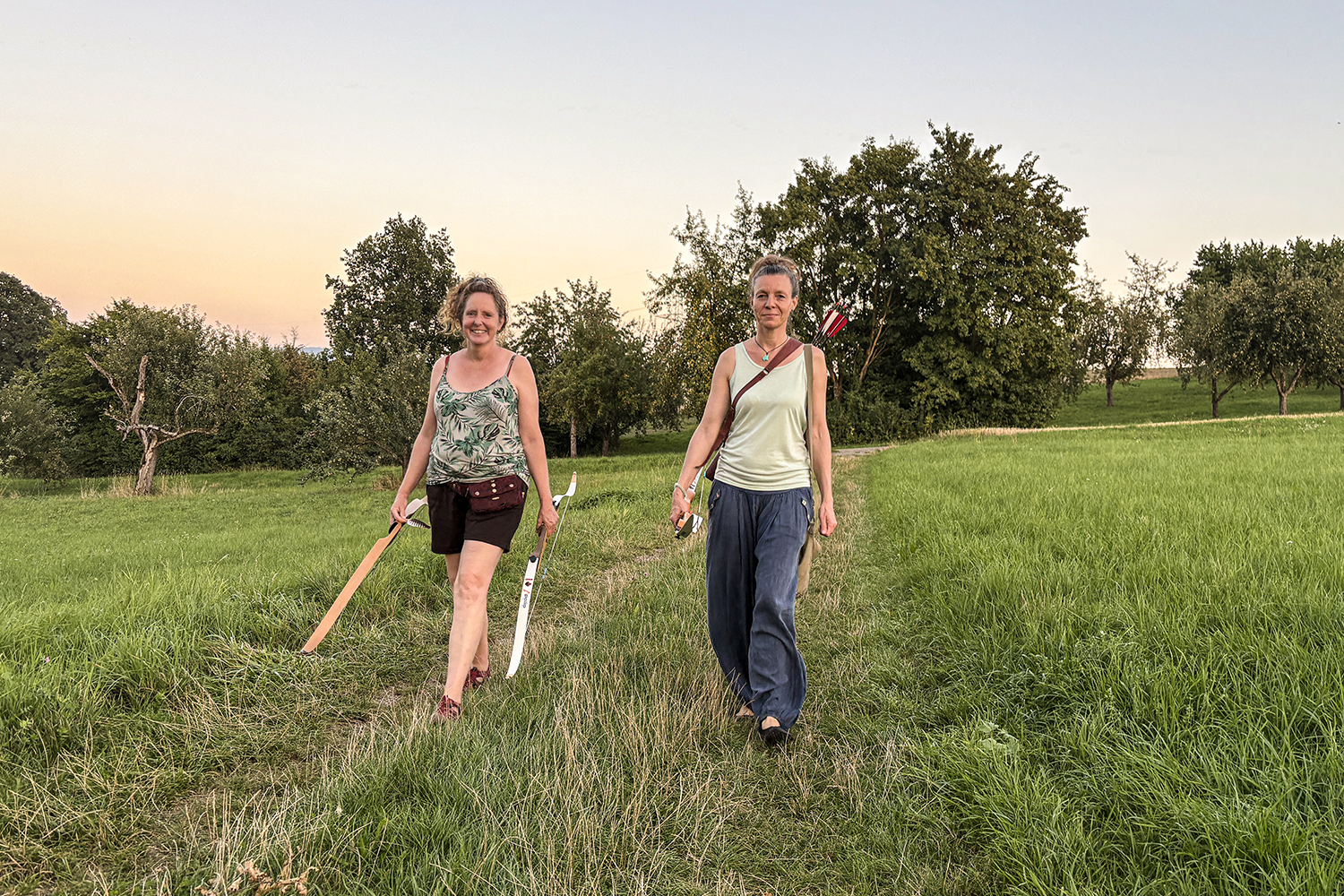 Anja mit KLientin auf dem Weg zum Bogenschießen über eine Wiese laufend