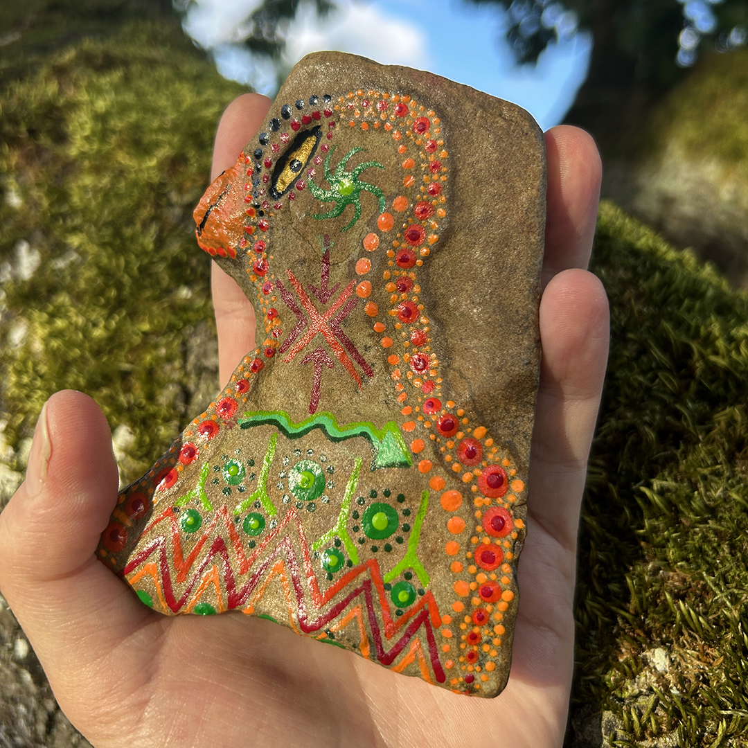 Indianischer Vogel auf einem Stein in Acrylfarbe gestaltet auf Moos in der Hand