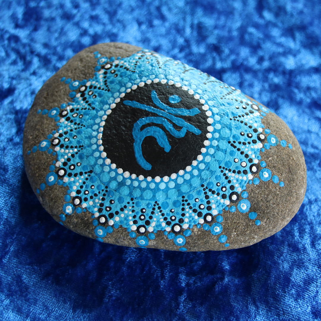 Symbol für Kehlchakra in Blautönen mit Acrylfarbe gestaltet auf Naturstein auf blauem Stoff