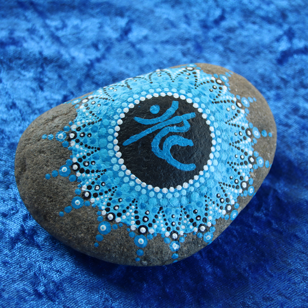 Symbol für Kehlchakra in Blautönen mit Acrylfarbe gestaltet auf Naturstein auf blauem Stoff
