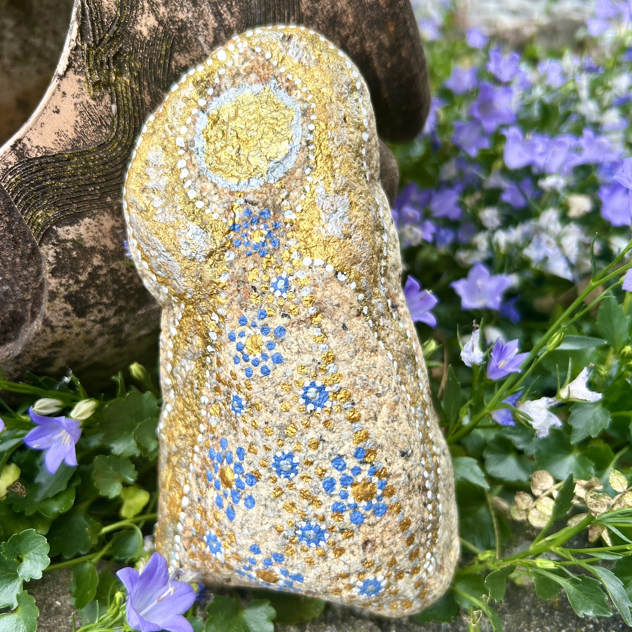 Engel auf Stein mit Acrylfarbe gestaltet vor Tonamphore und blauen Blumen