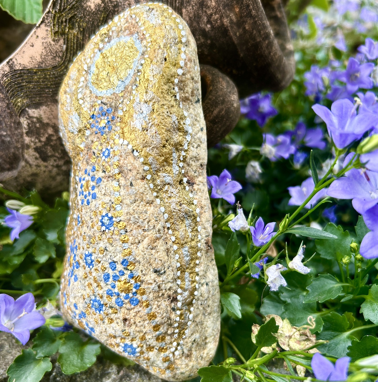 Engel auf Stein mit Acrylfarbe gestaltet vor Tonamphore und blauen Blumen
