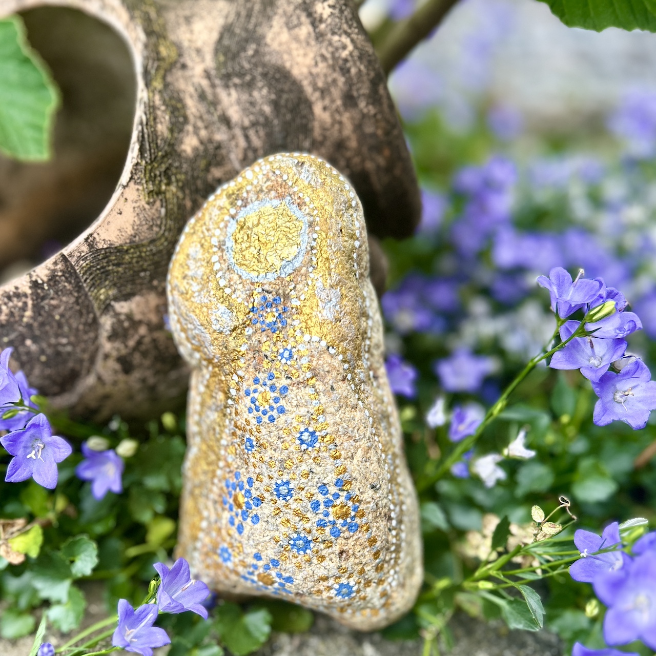 Engel auf Stein mit Acrylfarbe gestaltet vor Tonamphore und blauen Blumen