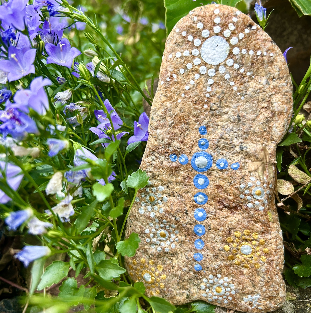 Rückseite des Engel auf Stein mit Acrylfarbe gestaltet vor Tonamphore und blauen Blumen Rückseite