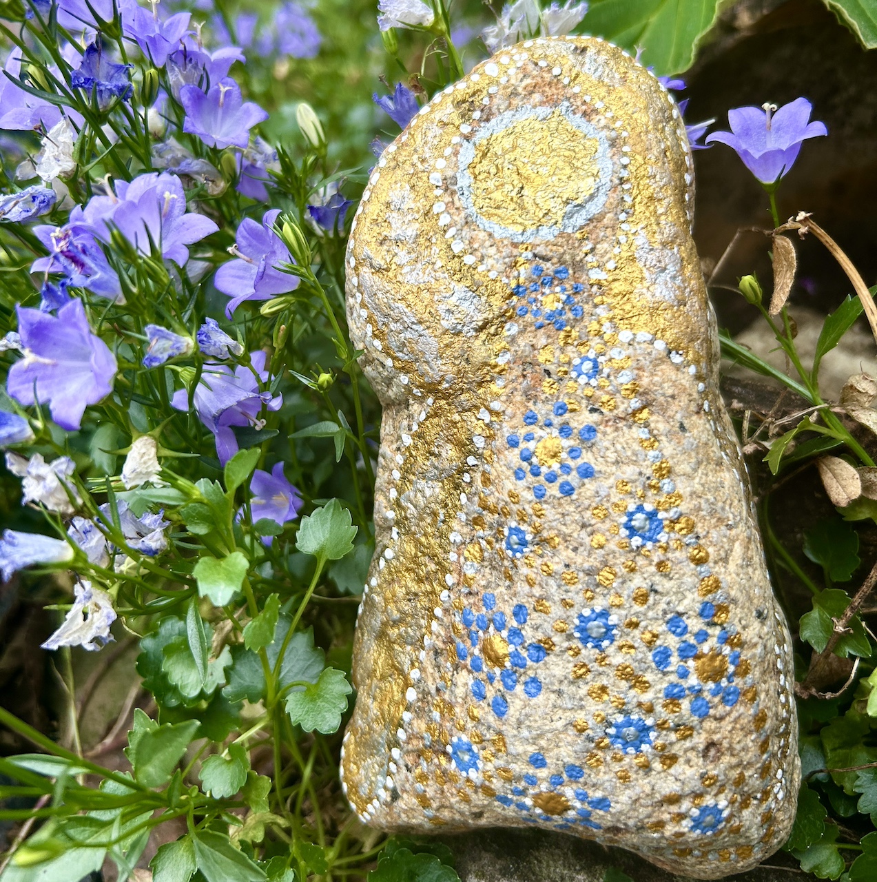 Engel auf Stein mit Acrylfarbe gestaltet vor Tonamphore und blauen Blumen 