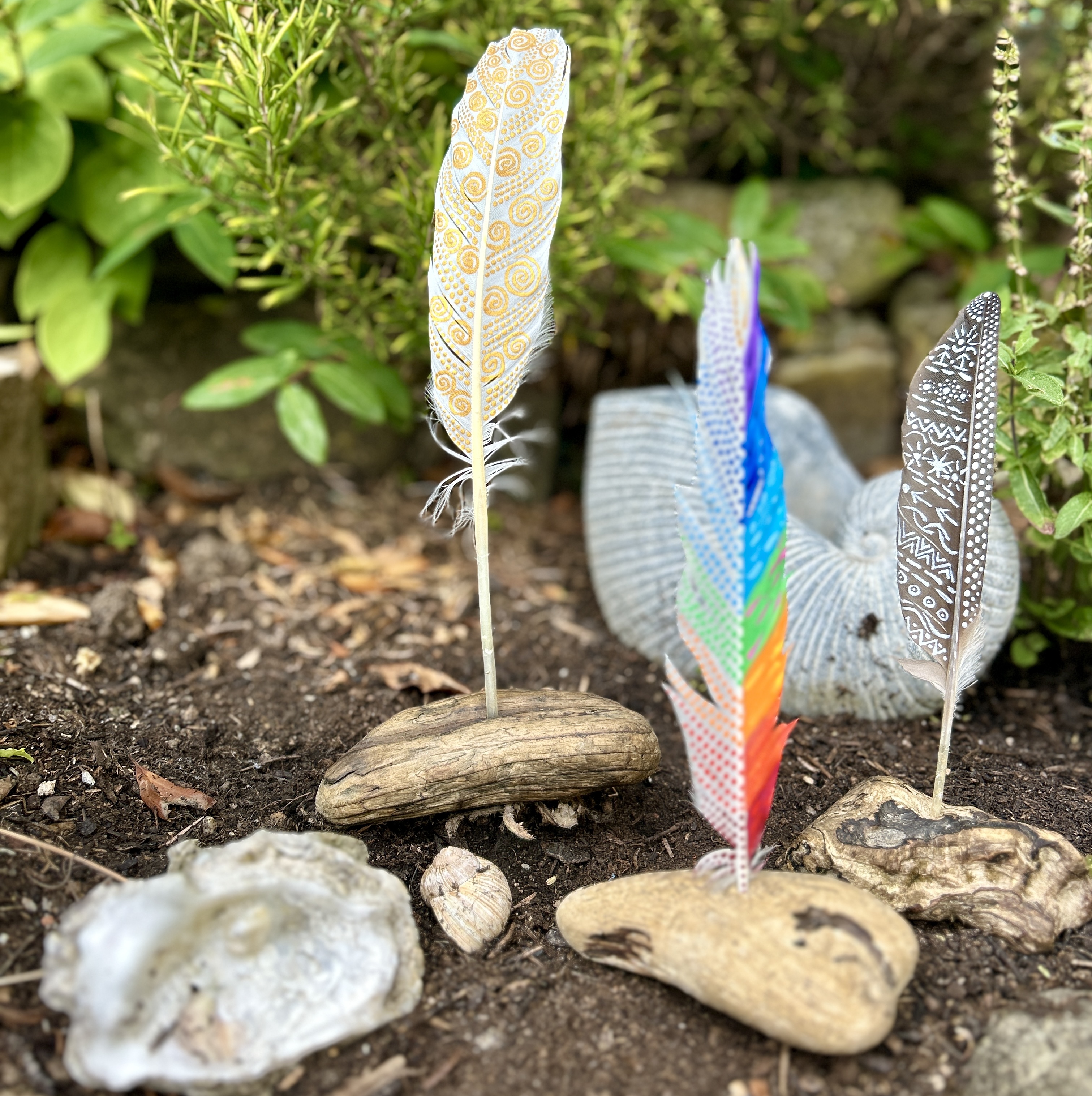 Drei bemalte Federn in Holzständern im Garten