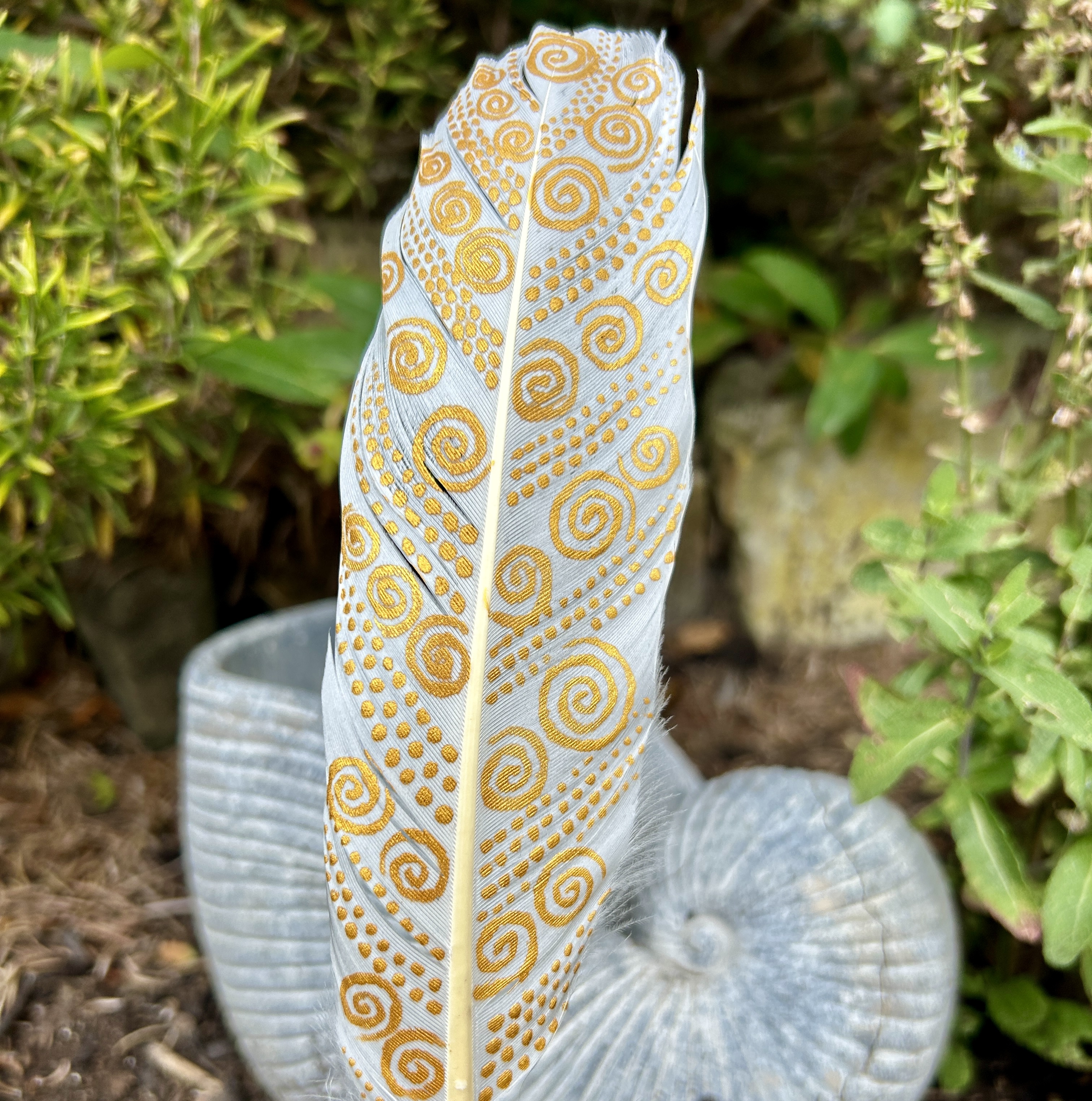 eine mit Gold bemalte Schwanenfeder in einem Holzständer im Garten