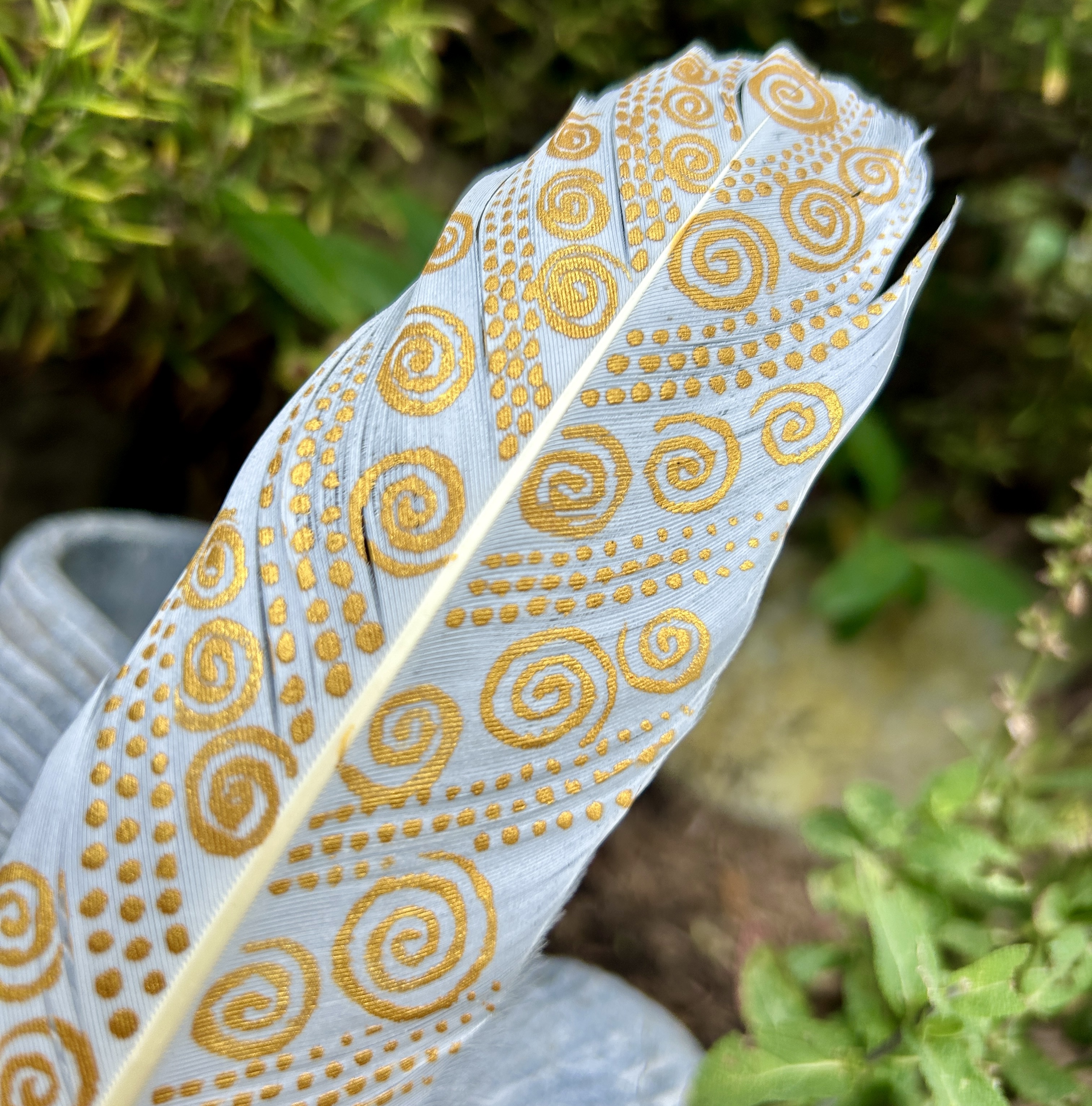 eine mit Gold bemalte Schwanenfeder in einem Holzständer im Garten
