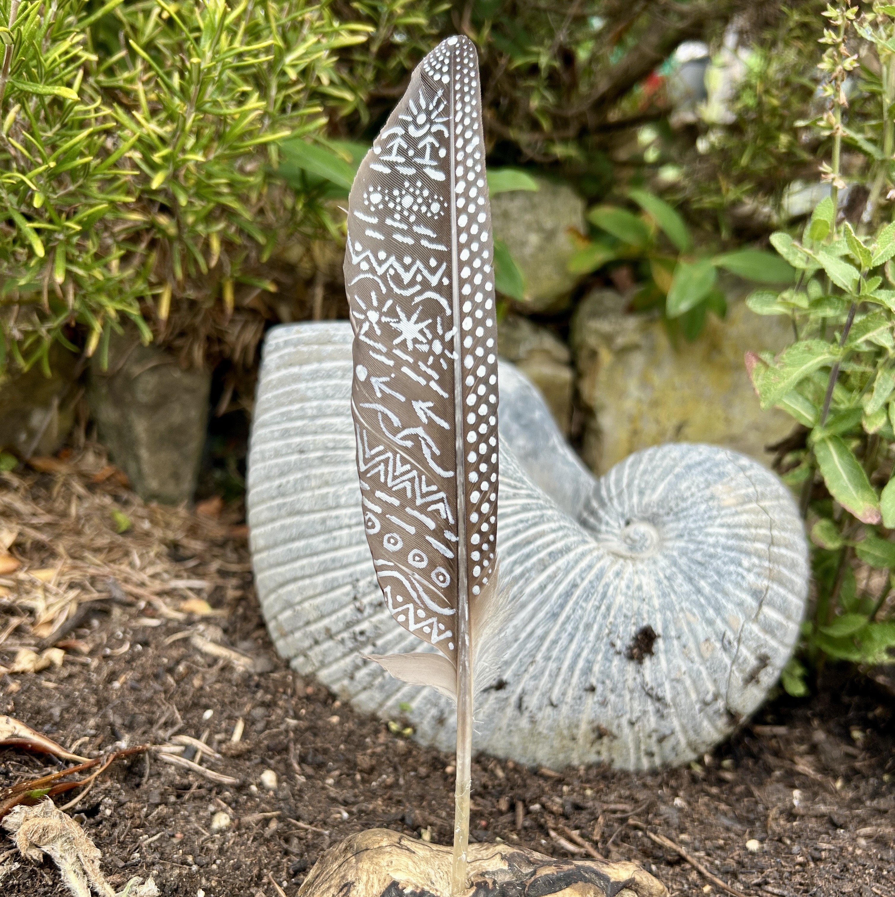 eine mit Silber bemalte dunkle Feder in einem Holzständer im Garten