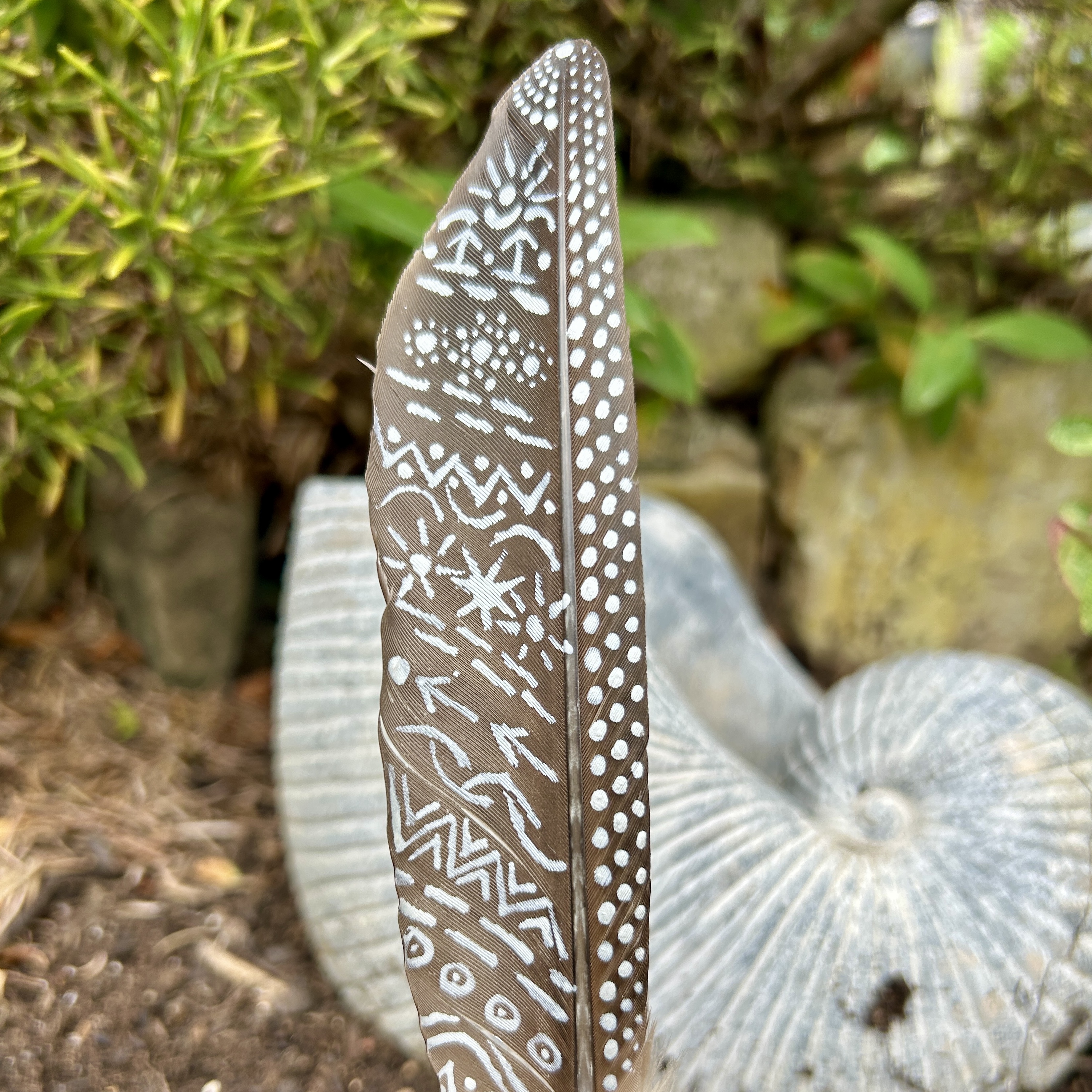 eine mit Silber bemalte dunkle Feder in einem Holzständer im Garten