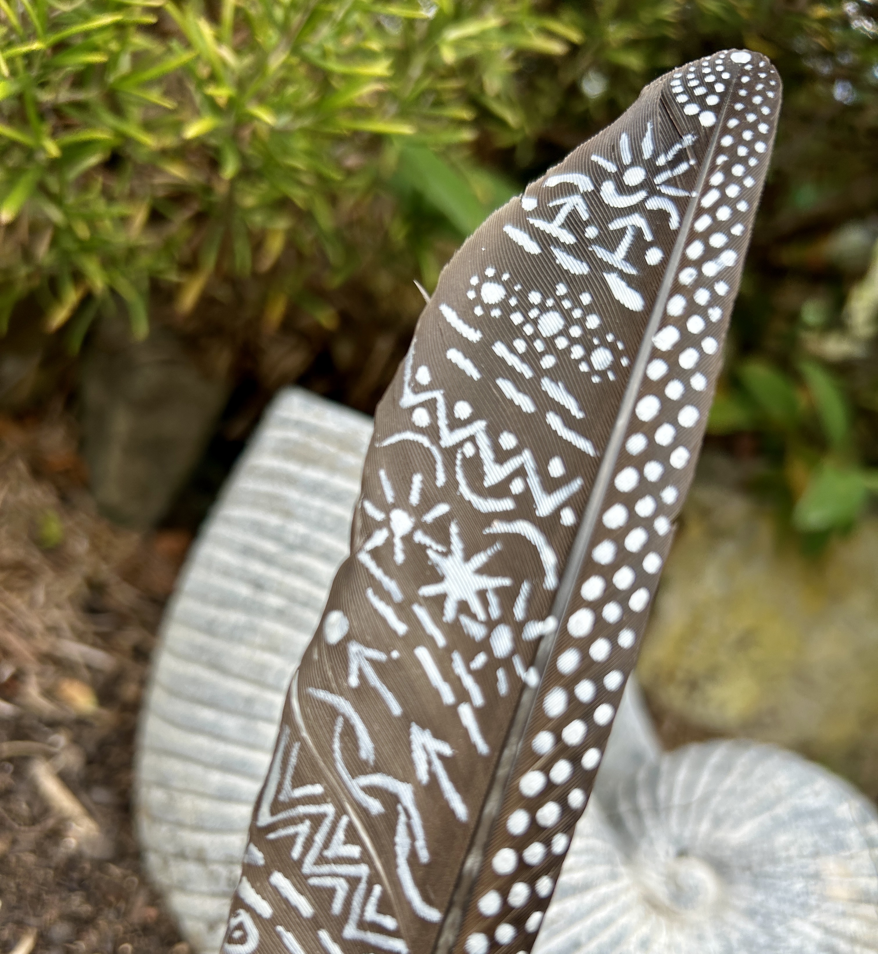 eine mit Silber bemalte dunkle Feder in einem Holzständer im Garten