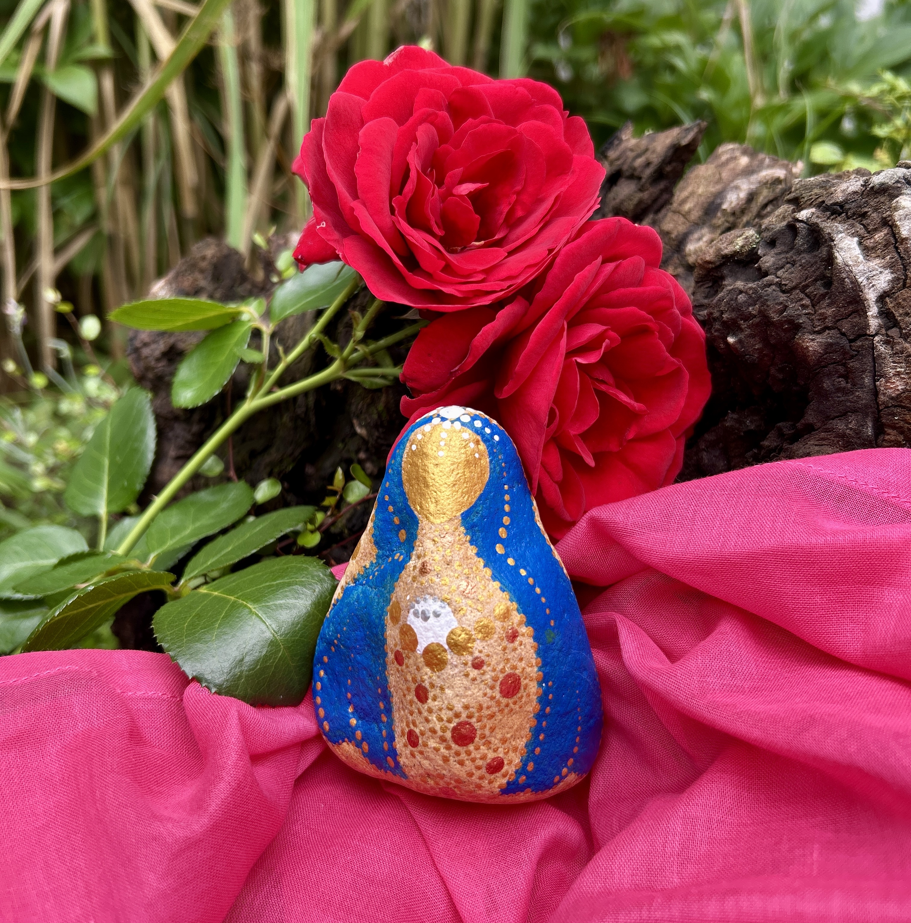 Stein mit Mutter Maria bemalt auf rosa Tuch vor roter Rose