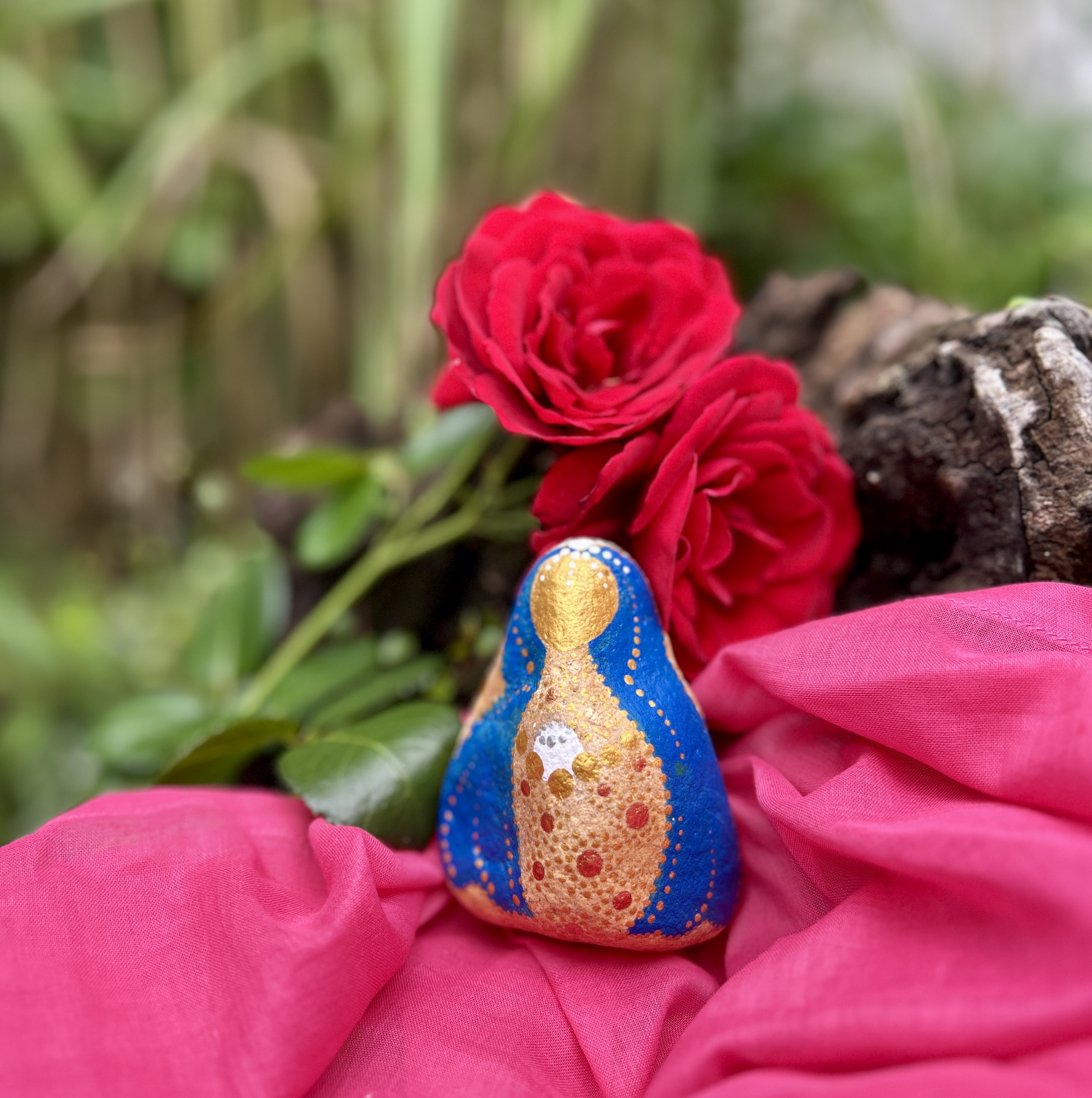 Stein mit Mutter Maria bemalt auf rosa Tuch vor roter Rose