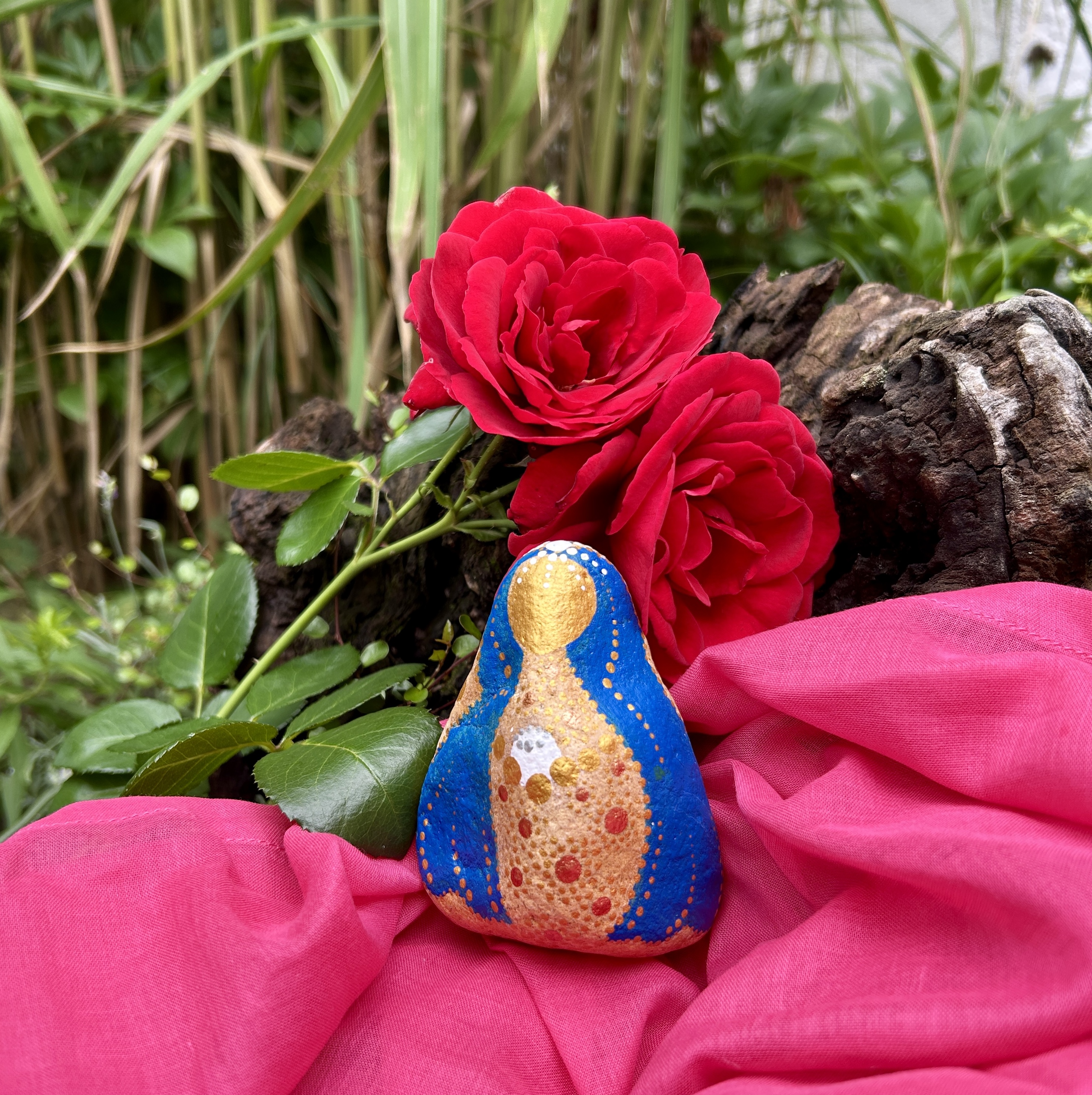 Stein mit Mutter Maria bemalt auf rosa Tuch vor roter Rose