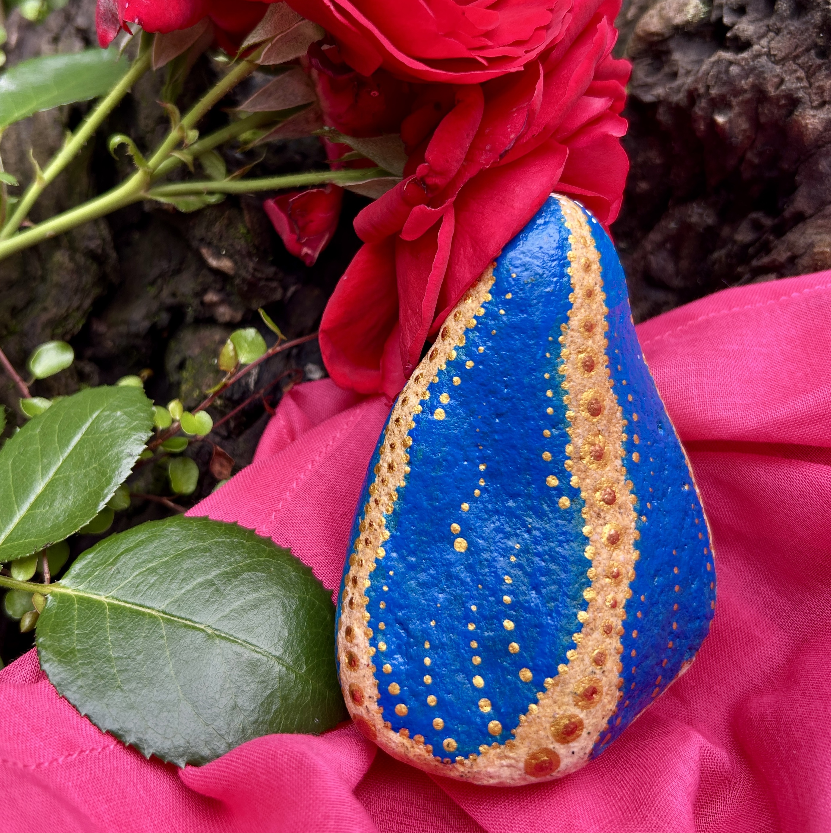 Stein mit Mutter Maria bemalt auf rosa Tuch vor roter Rose