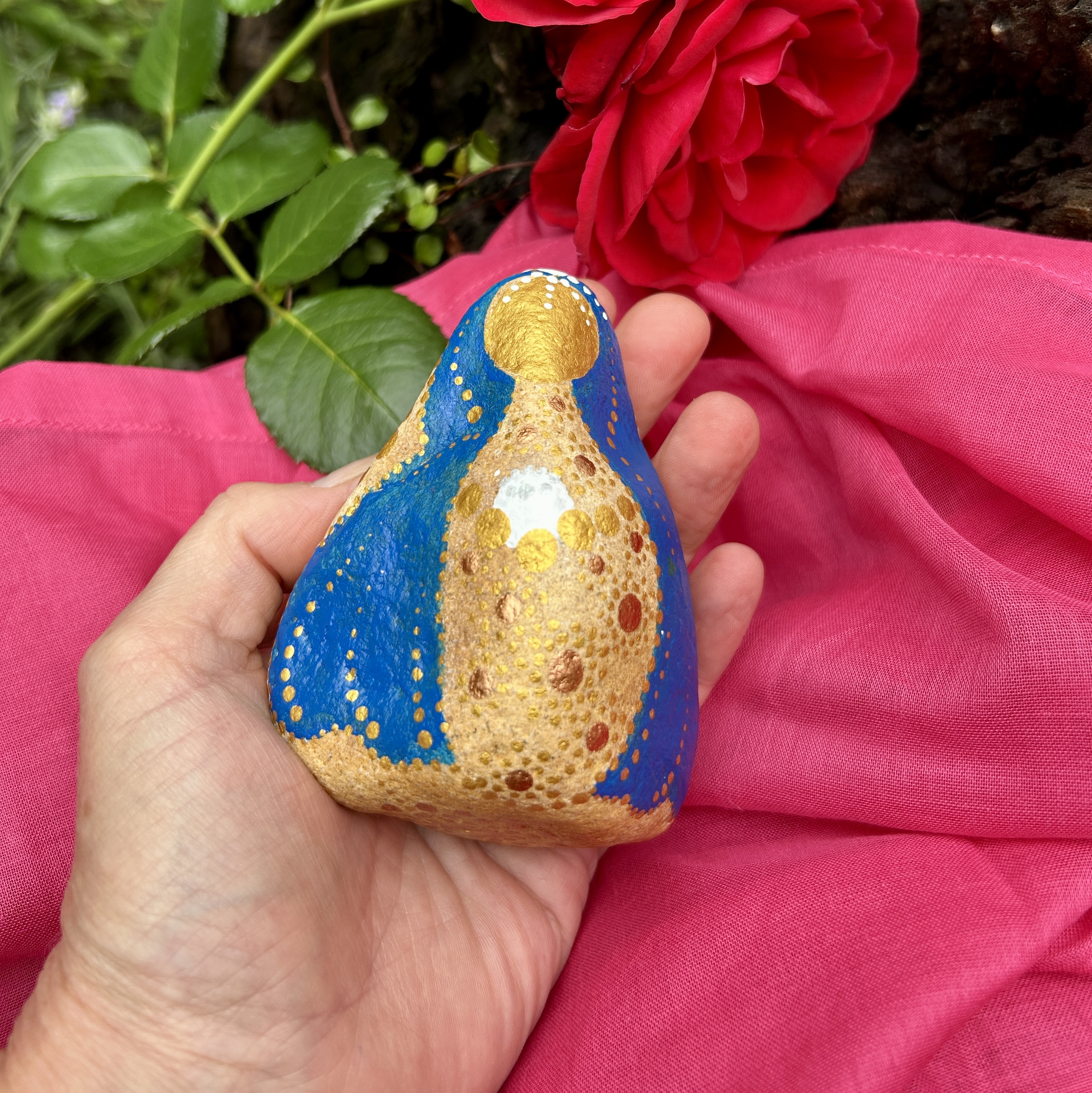 Stein mit Mutter Maria bemalt auf rosa Tuch vor roter Rose in der Hand gehalten
