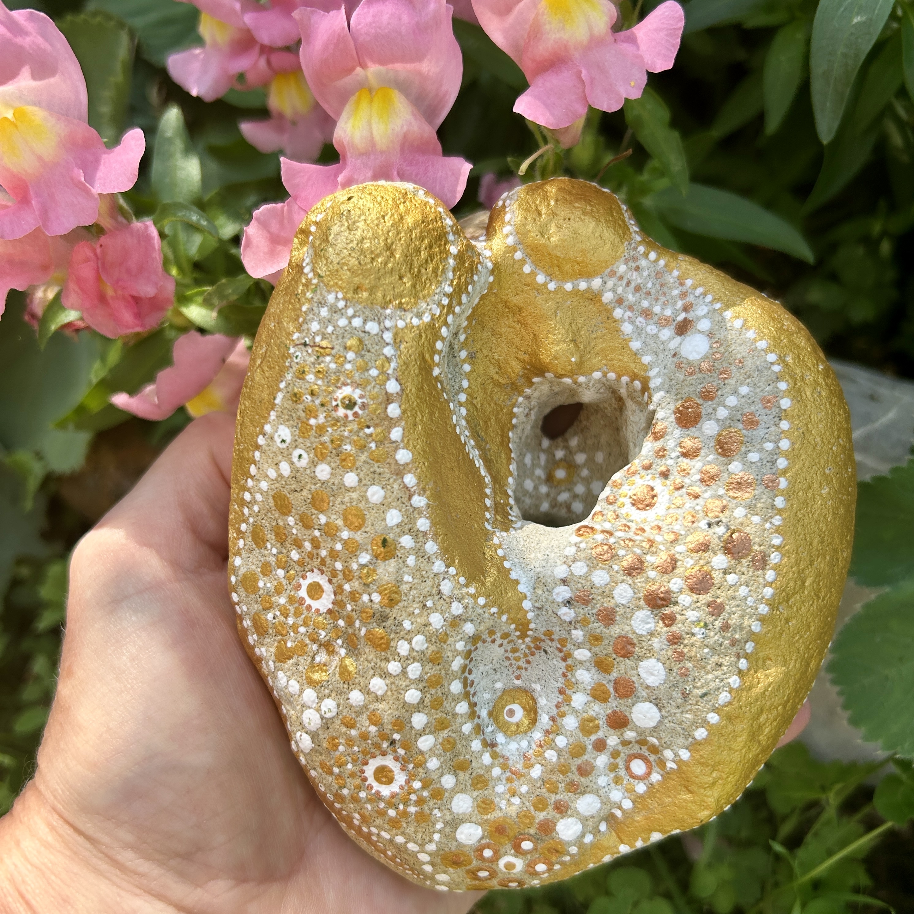 Bemalter Stein mit zwei Engeln in der Hand vor rosa Löwenmäulchen