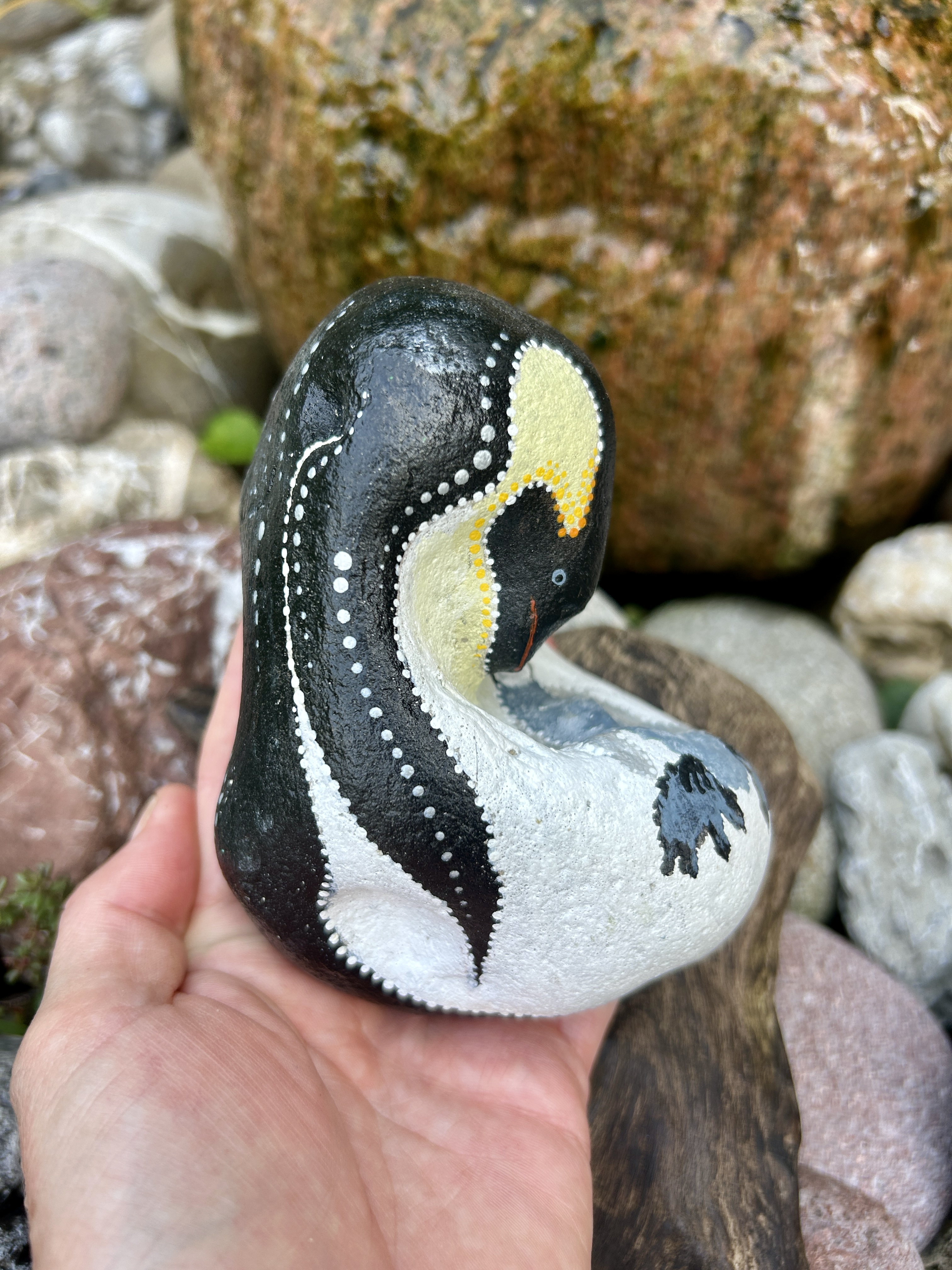 Bemalter Stein mit Pinguin von der Seite auf der Hand gehalten