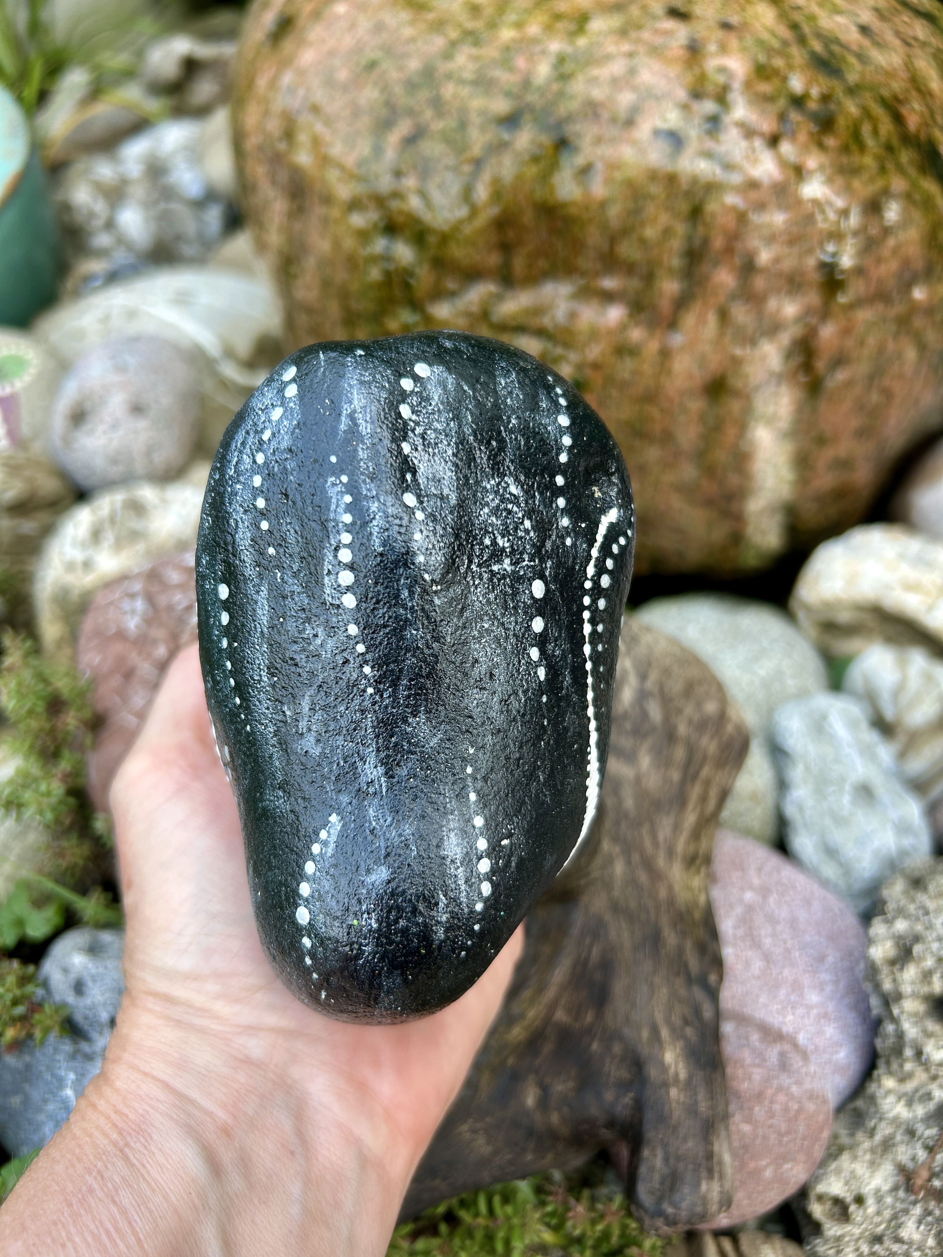 Bemalter Stein mit Pinguin von hintenauf der hand gehalten