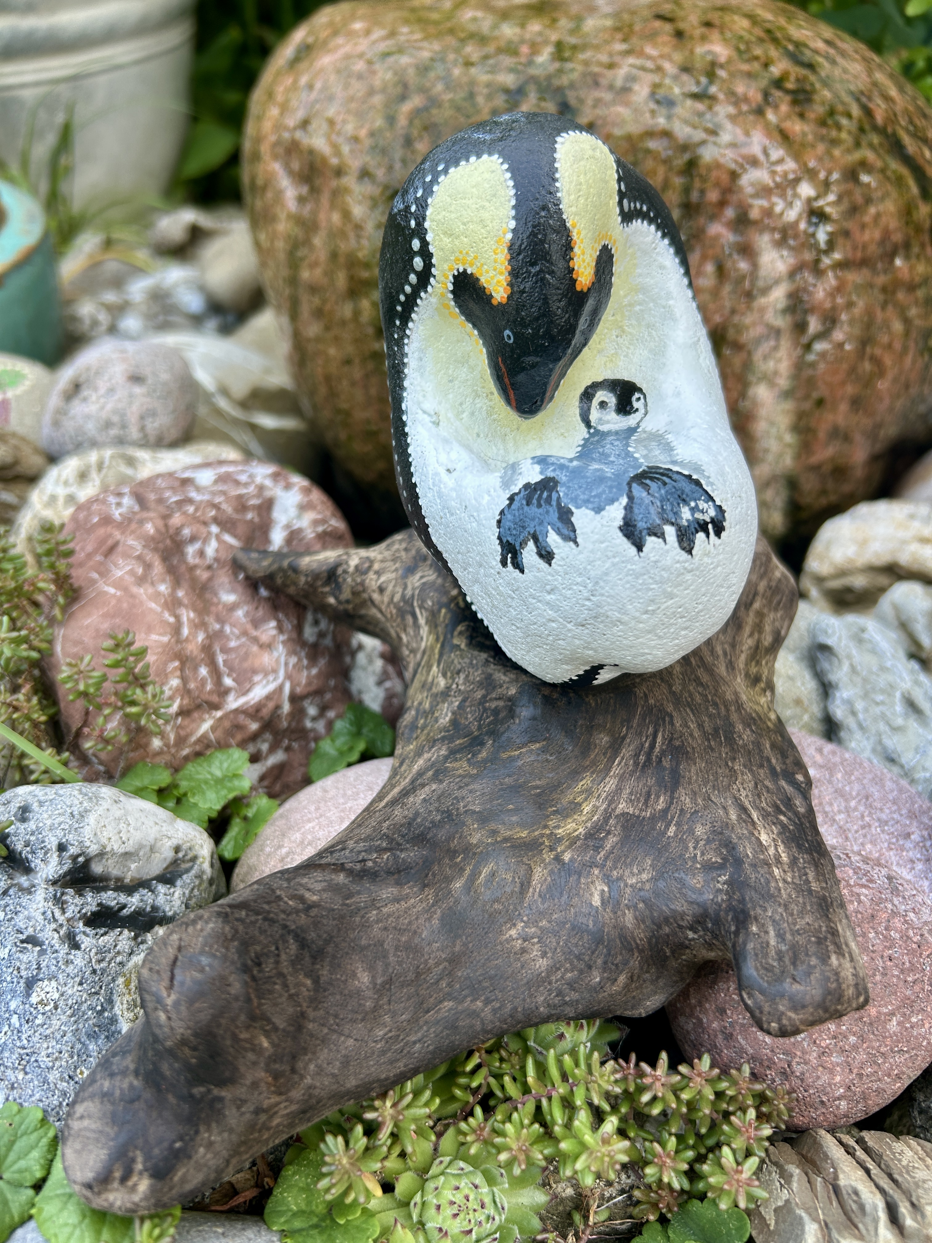 Bemalter Stein mit Pinguin und Junges auf einem Treibholzständer