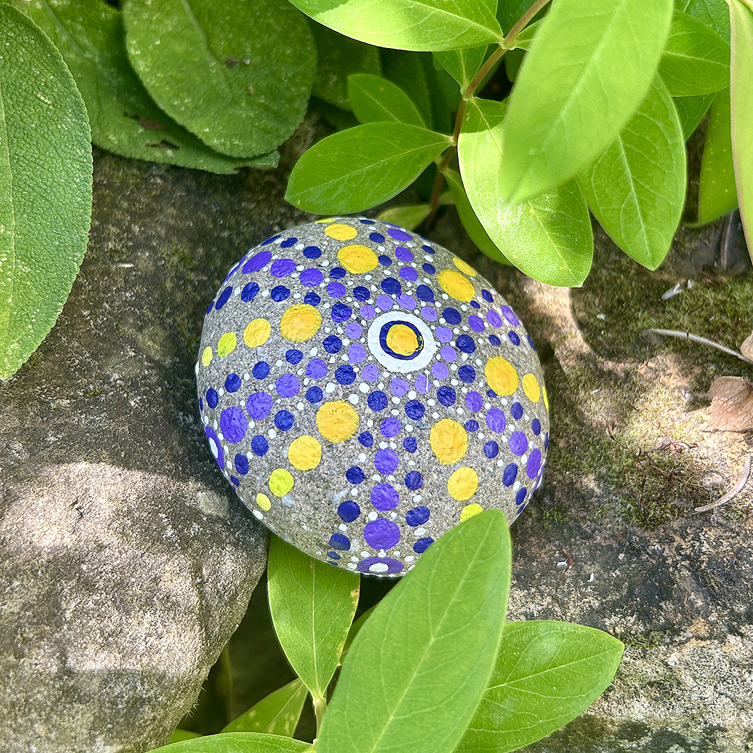 Bemalter Stein mit Mandala zwischen Blättern