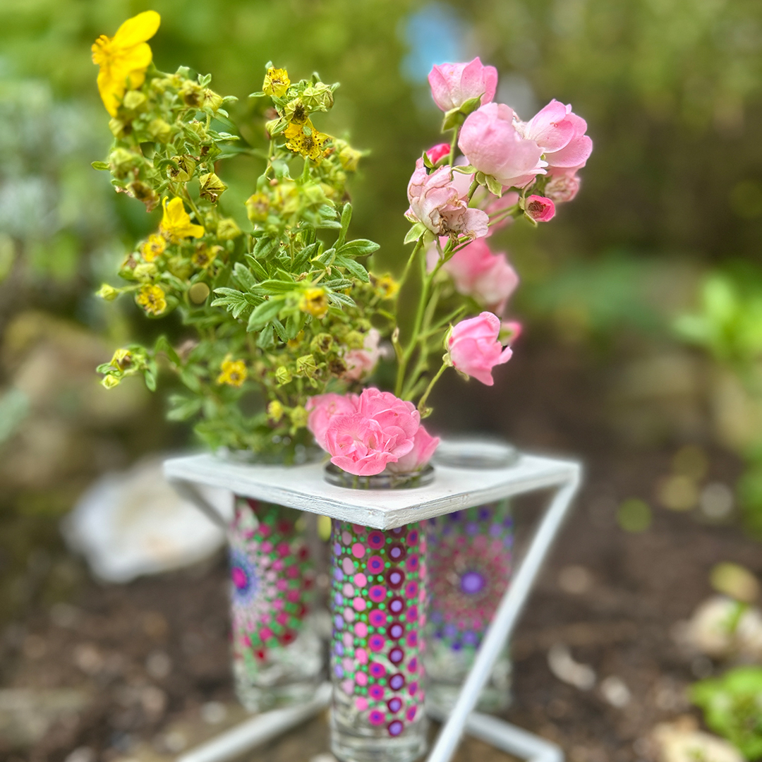 Glasvasen bemalt mit Mandalas in rosa und Violett mit gelben und rosa Blumen darin