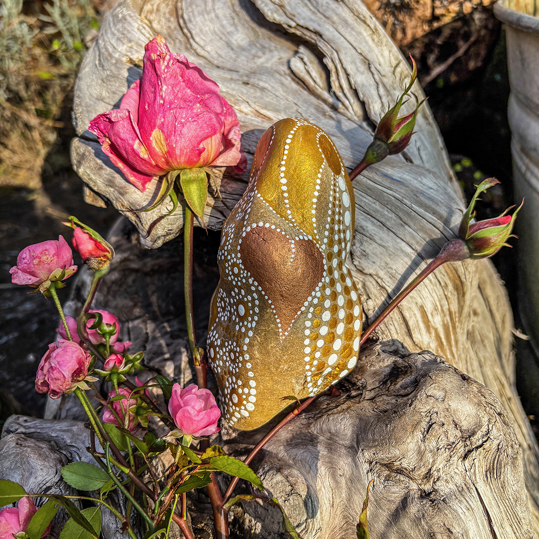 Bemalter Stein in weiß und Gold mit Rosen auf einer Wurzel