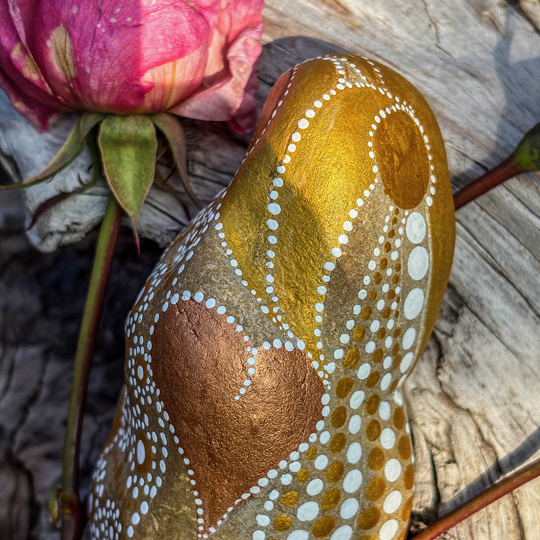 Bemalter Stein in weiß und Gold und einem Herz in Kupfer mit Rosen auf einer Wurzel