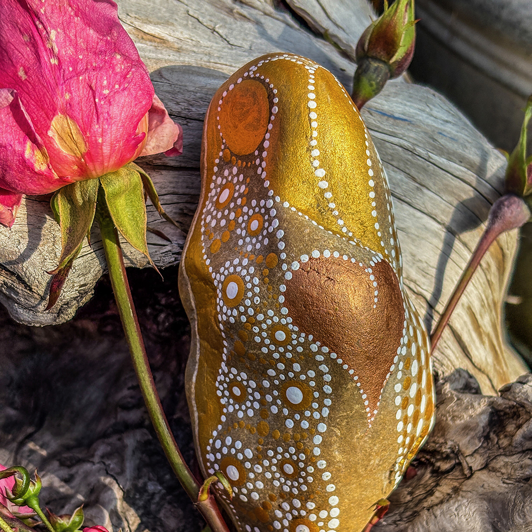 Bemalter Stein in weiß und Gold und einem Herz in Kupfer mit Rosen auf einer Wurzel
