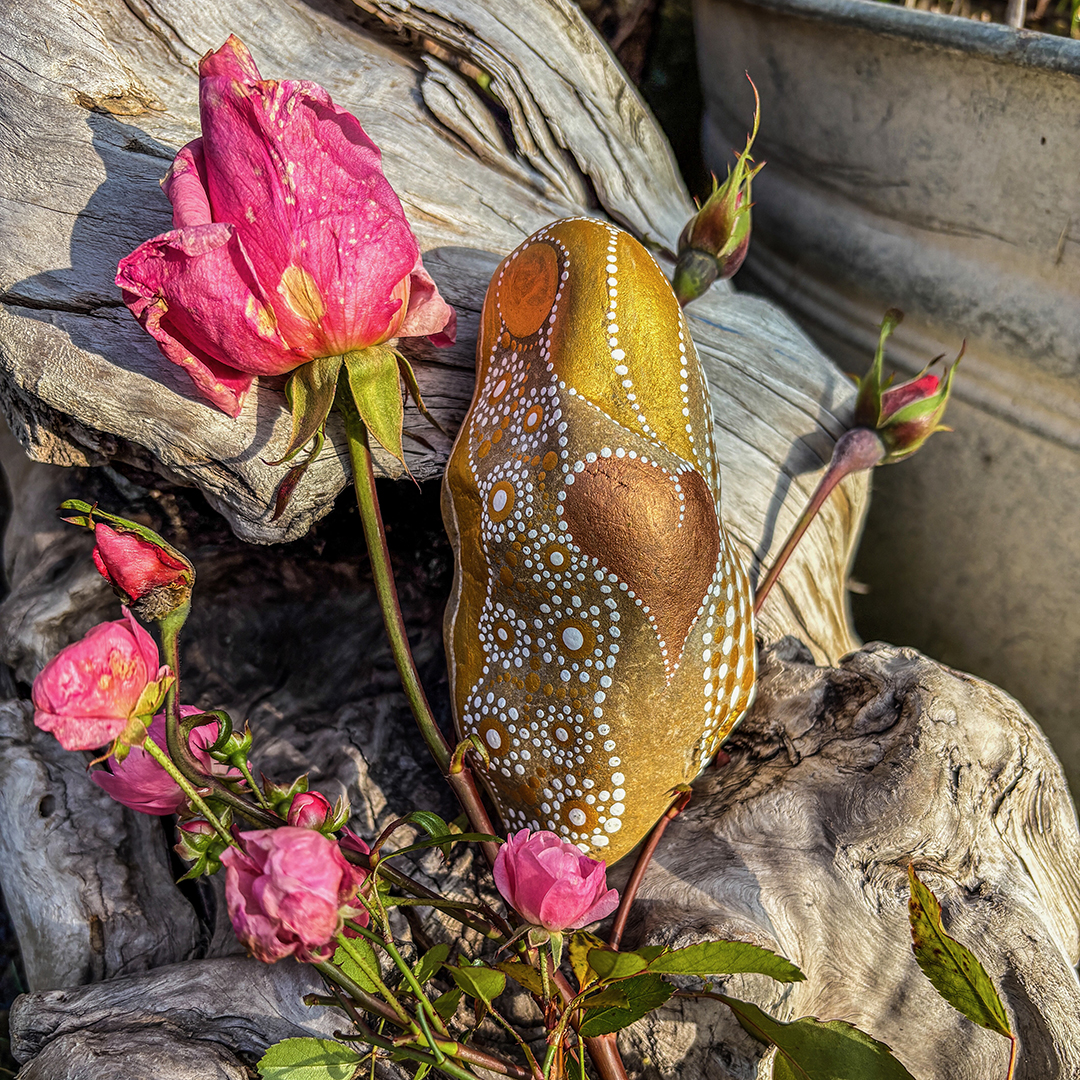 Bemalter Stein in weiß und Gold und einem Herz in Kupfer mit Rosen auf einer Wurzel
