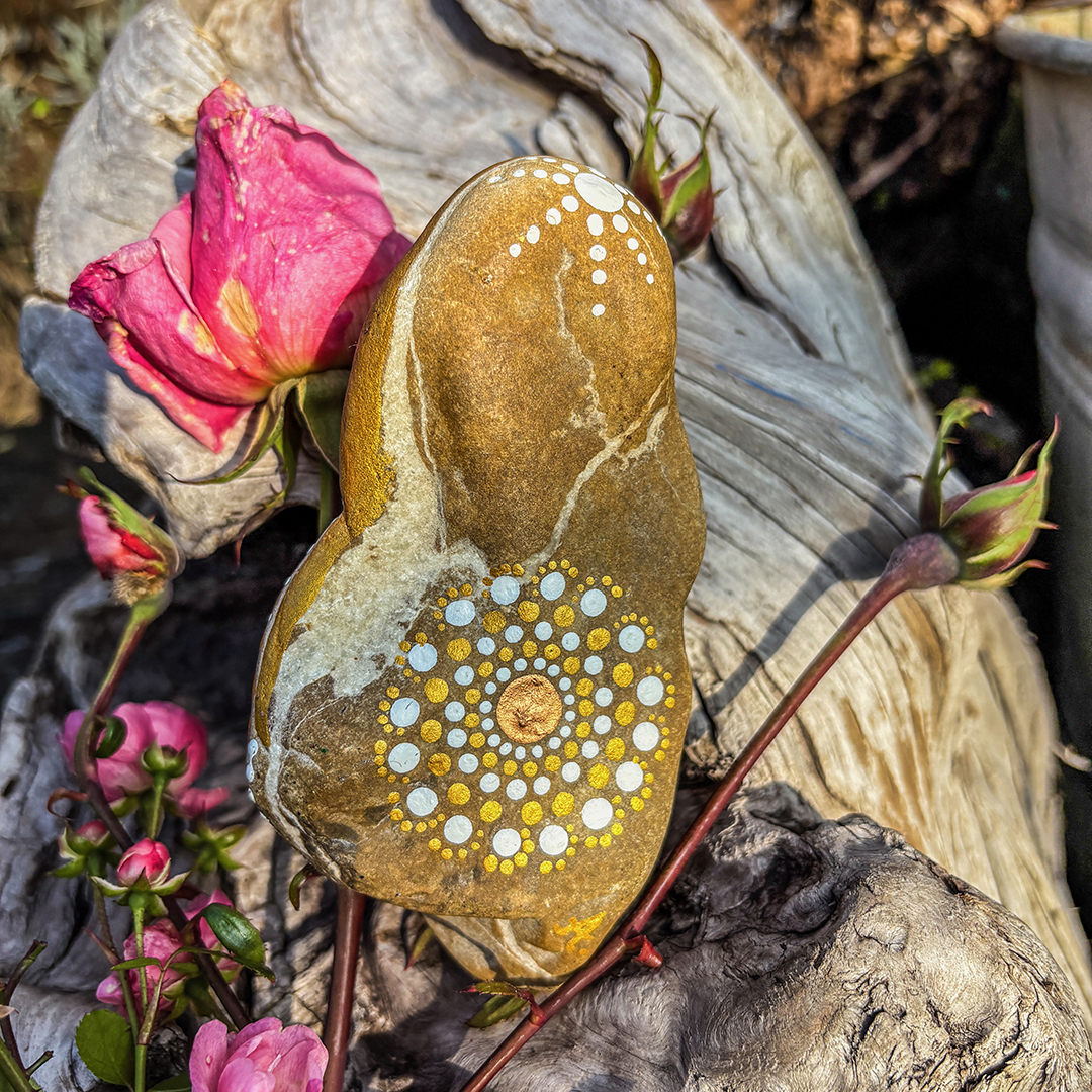 Mandala in weiß und Gold auf einem Stein vor Rosen und Wurzel