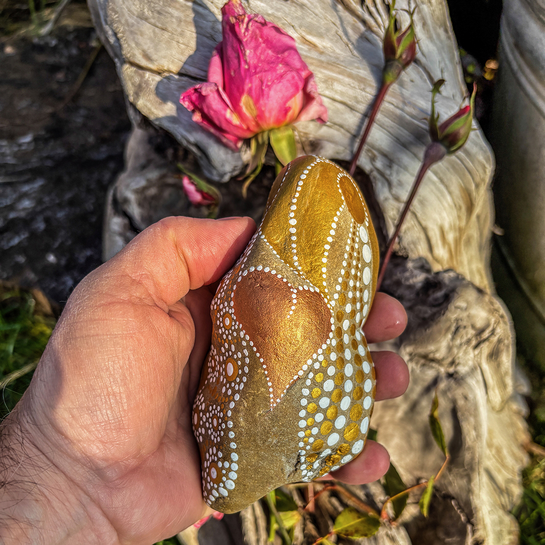 Hand, die einen bemalten Stein hält vor Rosen 