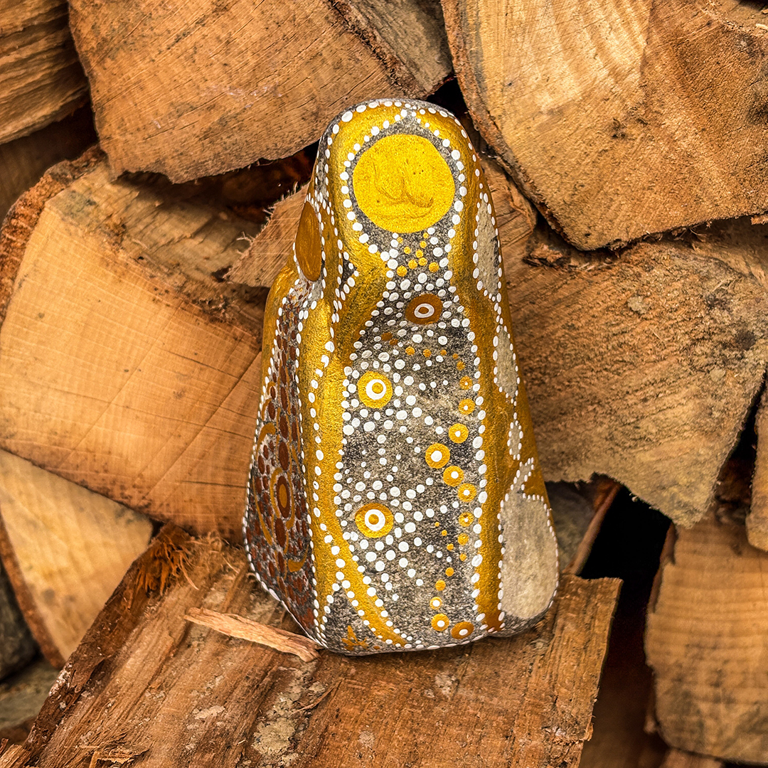 Stein mit Engel in Gold und Weiß bemalt vor Holzscheiten