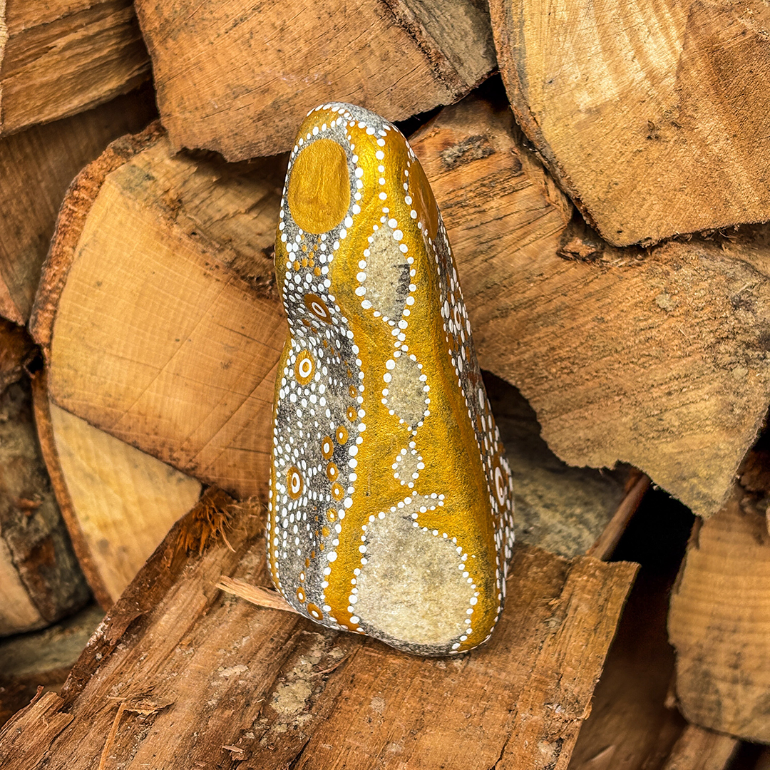 Stein mit Engel in Gold und Weiß bemalt vor Holzscheiten