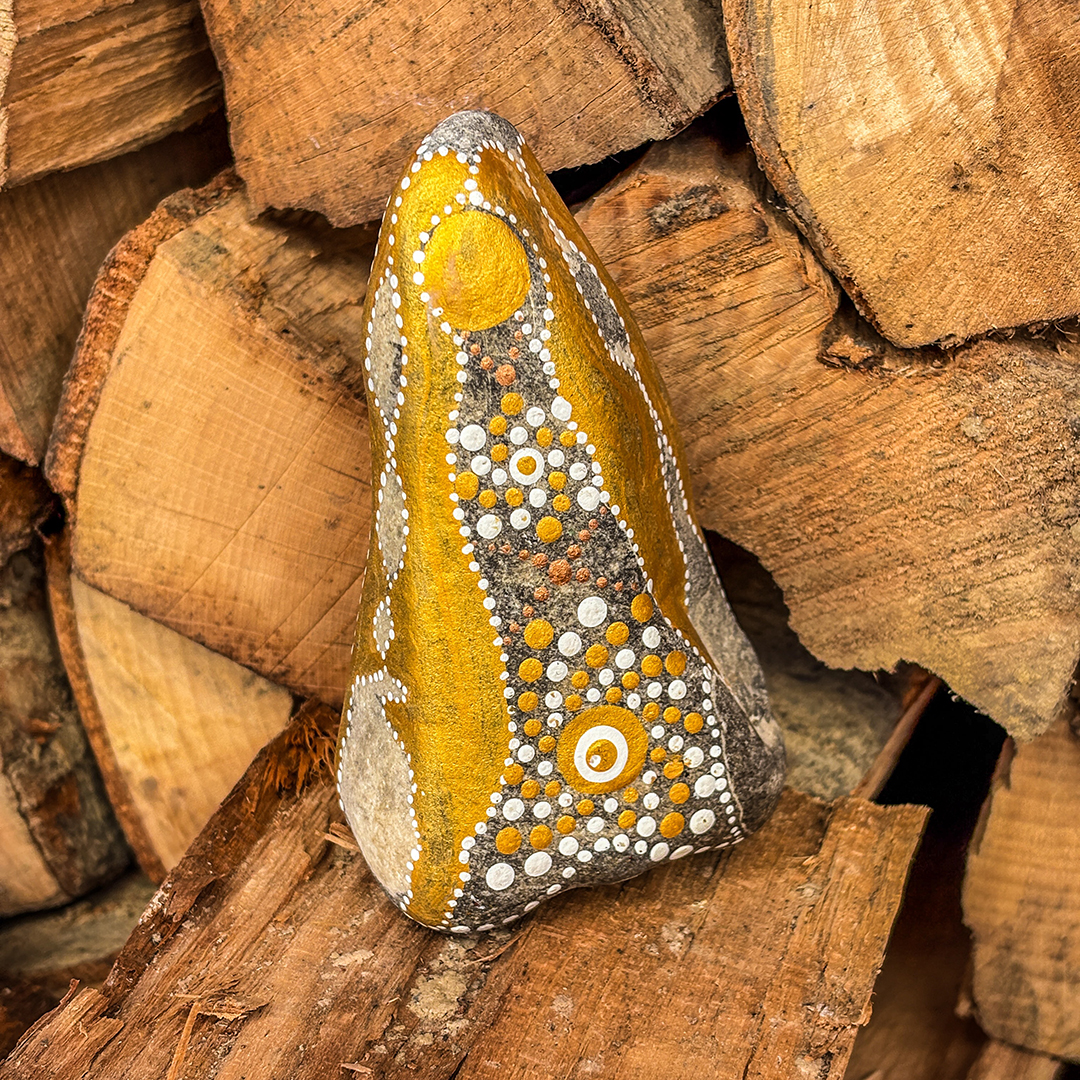 Stein mit Engel in Gold und Weiß bemalt vor Holzscheiten