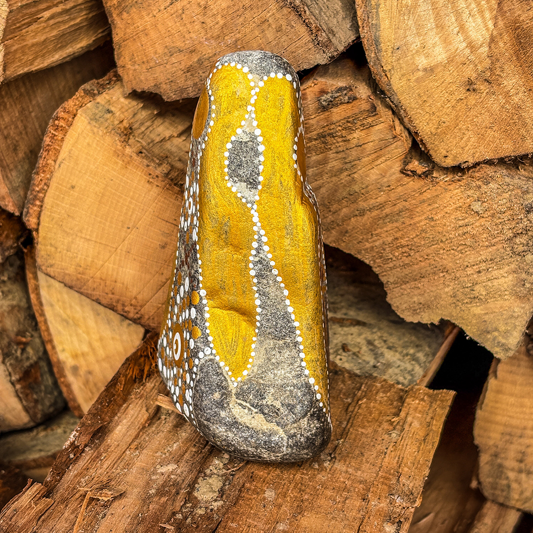 Stein mit Engel in Gold und Weiß bemalt vor Holzscheiten