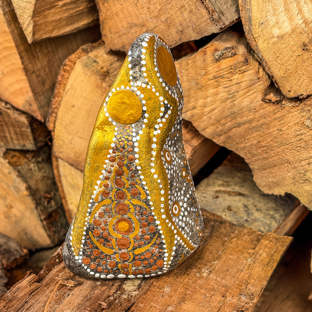 Stein mit Engel in Gold und Weiß bemalt vor Holzscheiten