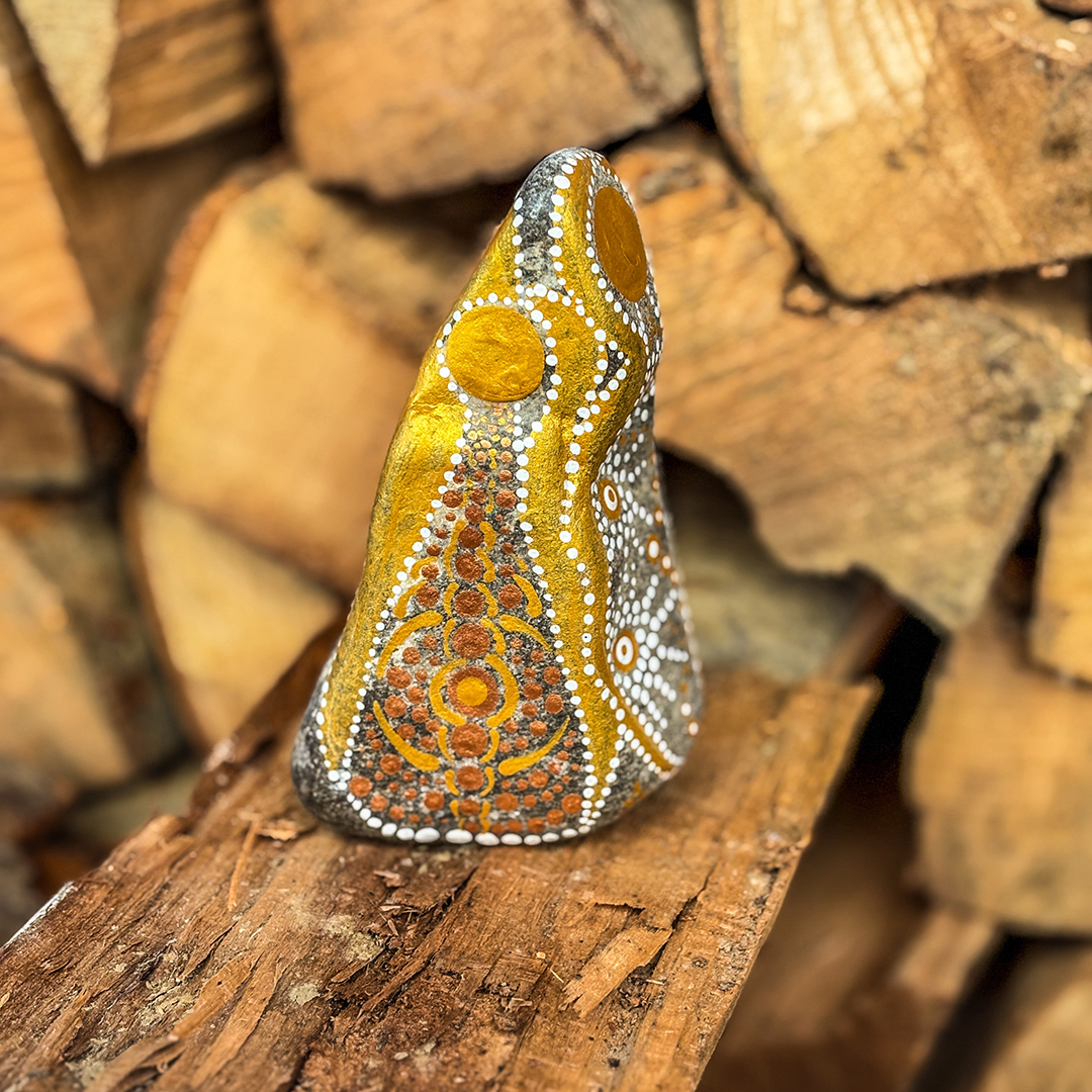 Stein mit Engel in Gold und Weiß bemalt vor Holzscheiten