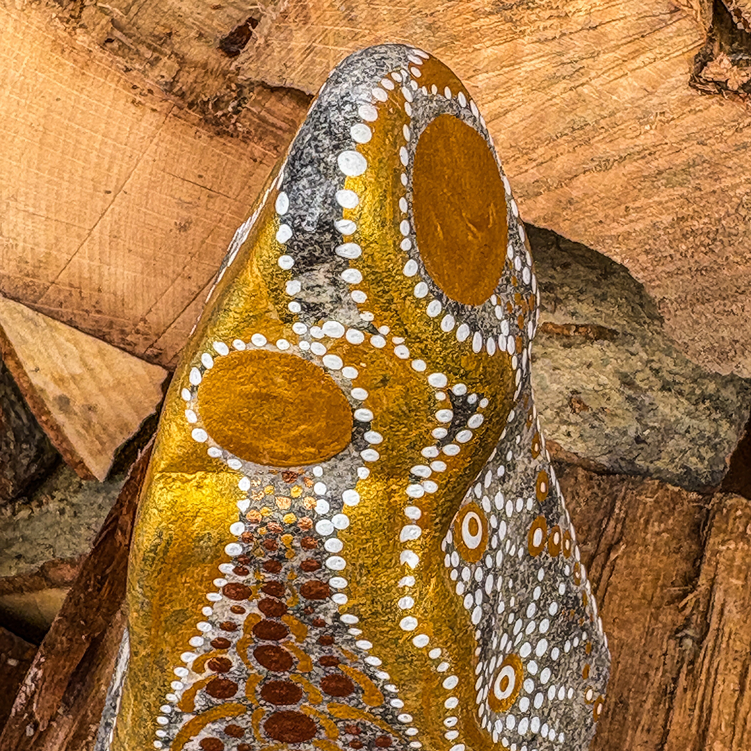 Nahaufnahme von Stein mit Engel in Gold und Weiß bemalt vor Holzscheiten