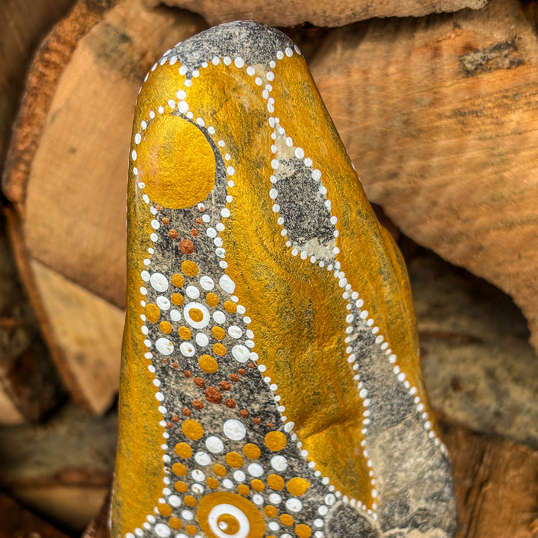 Stein mit Engel in Gold und Weiß bemalt vor Holzscheiten