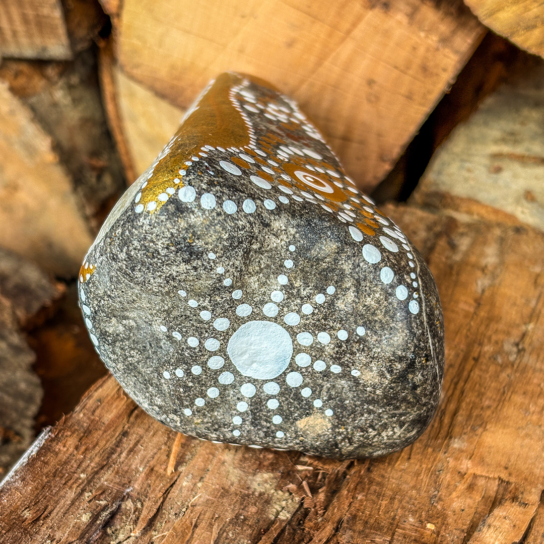 Unterseite von Stein mit Engel in Weiß bemalt vor Holzscheiten