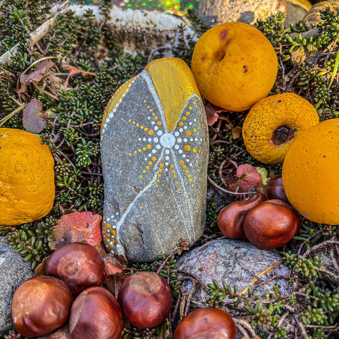 Stein bemalt in Gold und Weiß zwischen Zierpfirsichen und Kastanien liegend