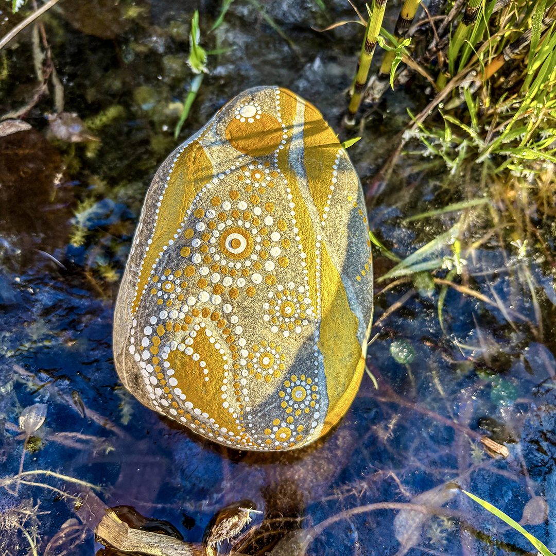 Stein bemalt mit einem Engel in Gold und Weiß auf gefrorenem Wasser liegend