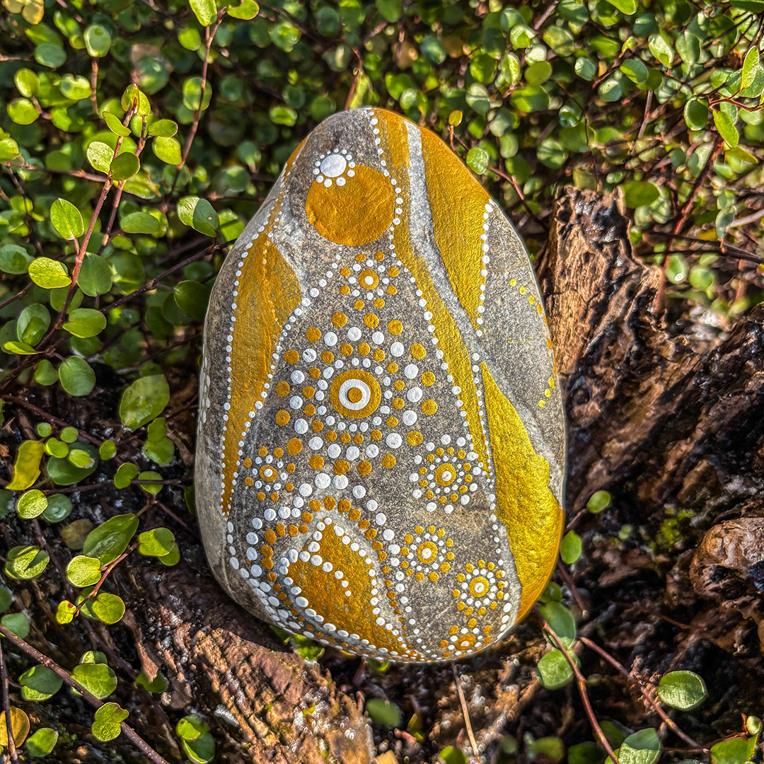 Stein bemalt mit einem Engel in Gold und Weiß auf einer Wurzel 