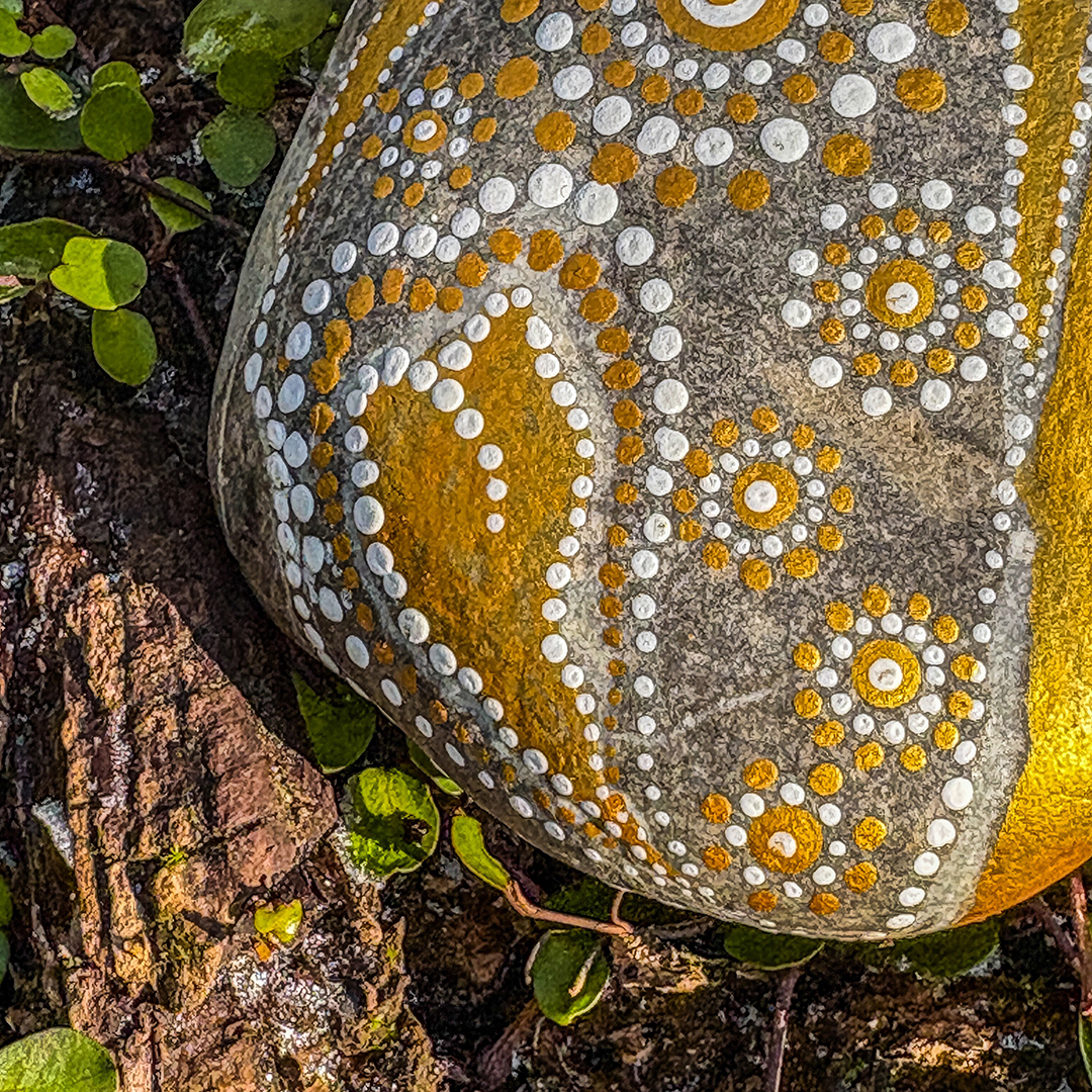 Nahaufnahme von einem Stein bemalt mit einem Herz in Gold und Weiß 