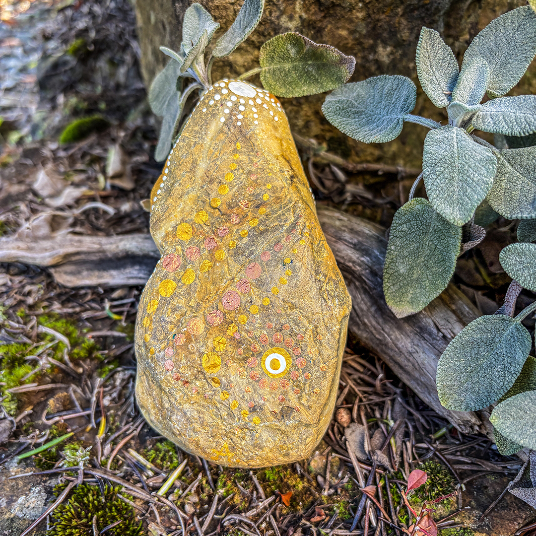 Stein bemalt in Gold und Weiß in Dot Painting Technik vor Steinen, Blättern und Ast
