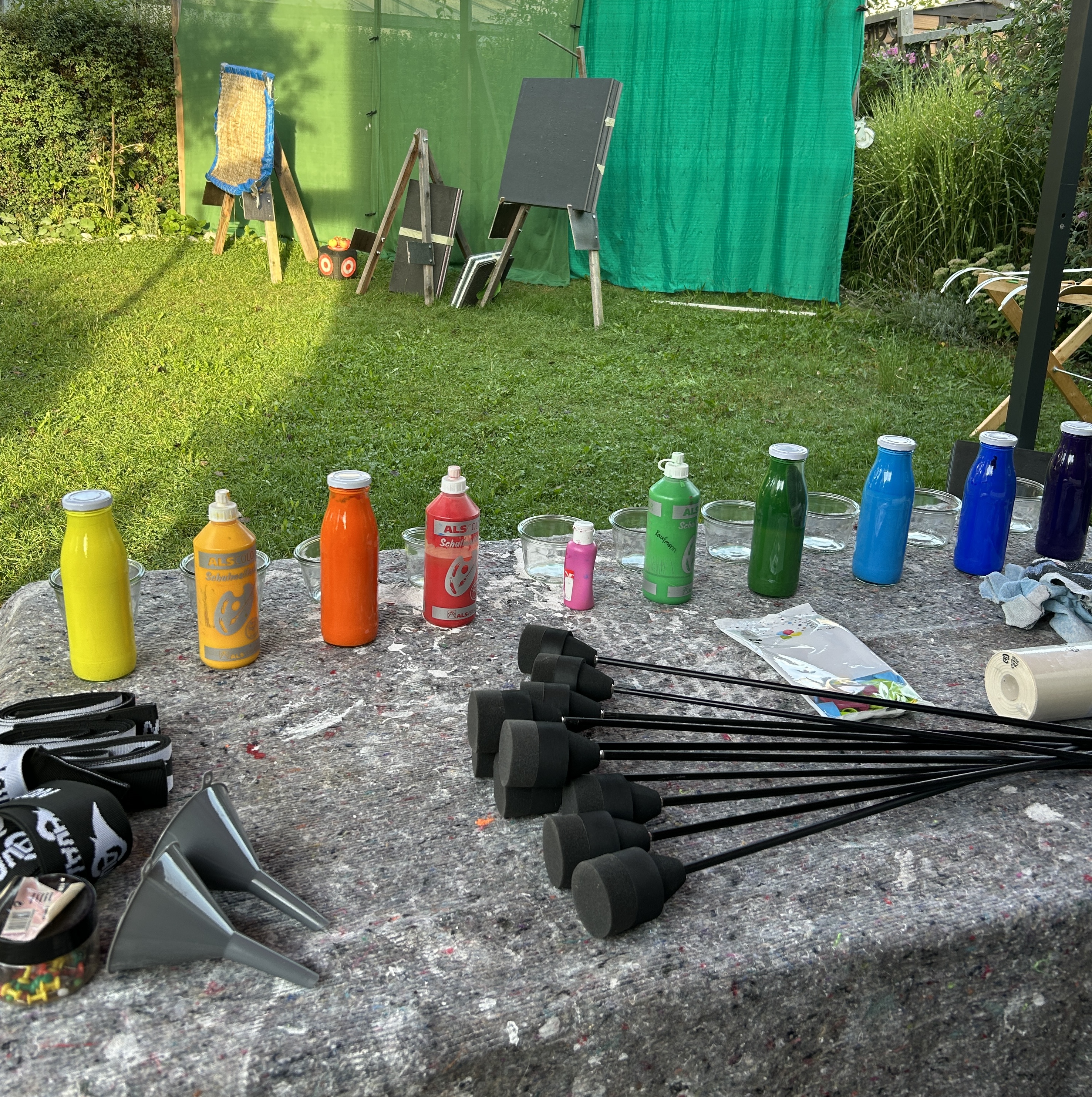 Farbflaschen und Pfeile auf einem Tisch im Garten vor Zielscheiben
