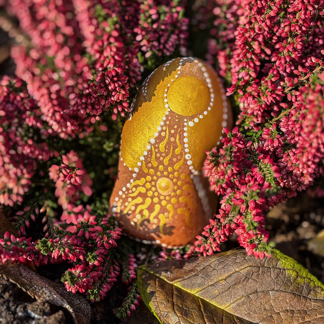 Bemalter Stein mit Engel in roter Erikapflanze