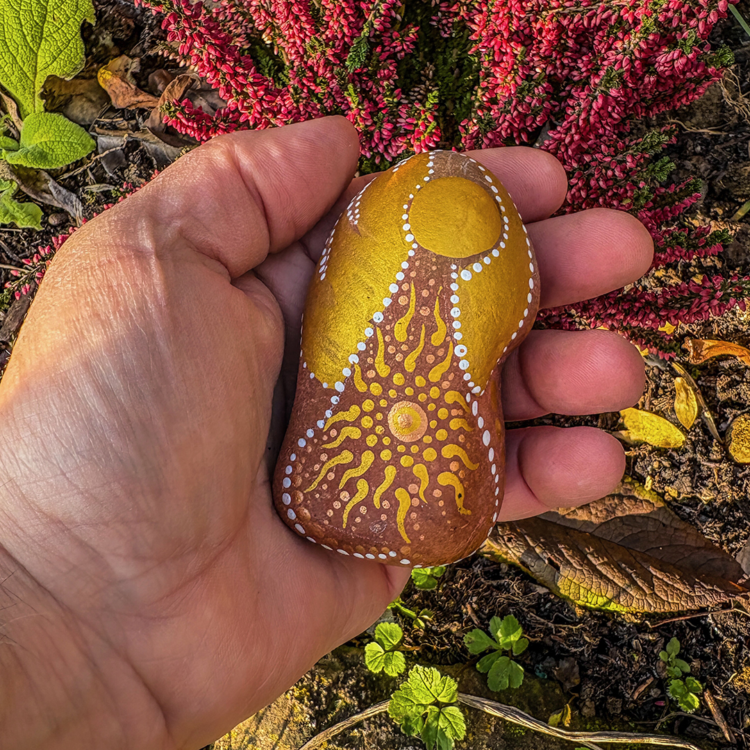 Bemalter Stein mit Engel in Hand gehalten vor roter Erika